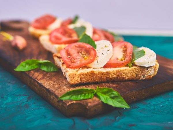 Caprese bruschetta toasts on cutting board. Bruschetta with tomatoes, mozzarella cheese and basil on a green background. Traditional italian appetizer or snack, antipasto